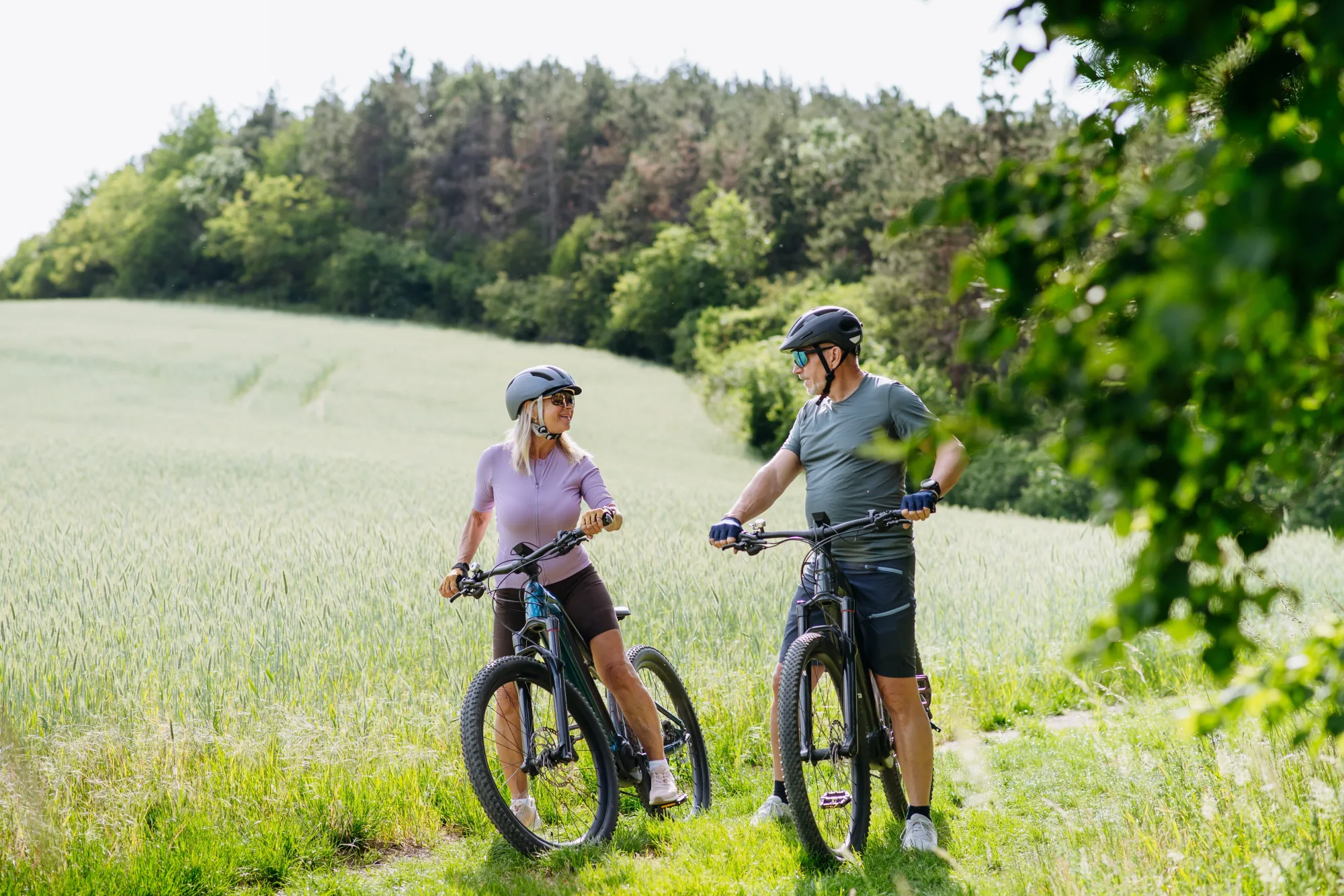 Paar mit E-Bikes bei einer Pause in grüner Landschaft